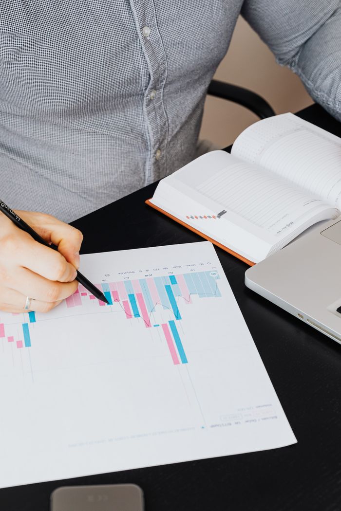 Close-up of a person analyzing a graph with a laptop and notebook for business planning.