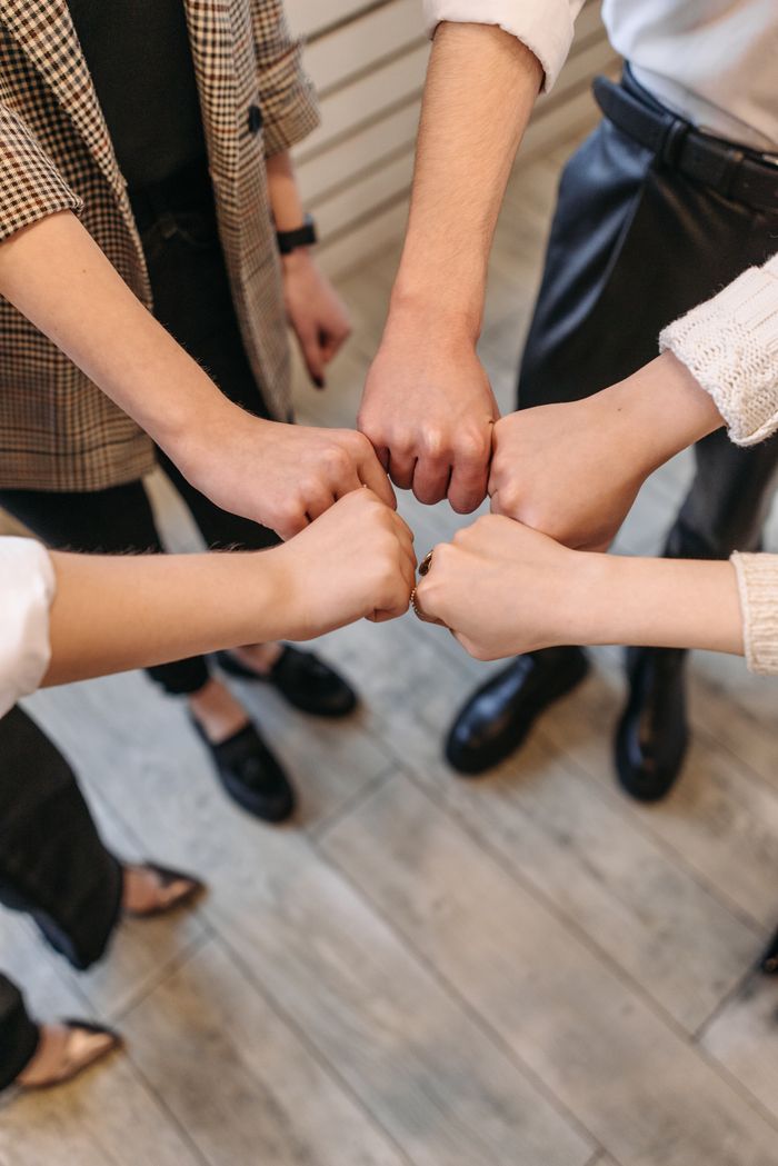 A close-up of five people fist bumping, symbolizing teamwork and unity indoors.